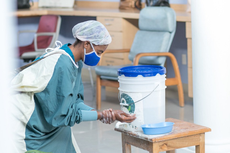 A woman wears PPE and she washes her hands at a handwashing station in Haiti in July 2020