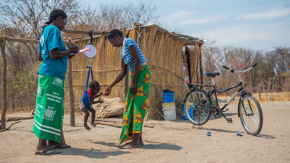 A community health worker with a mother and her child being weighed for malnourishment in Zambia in October 2019.