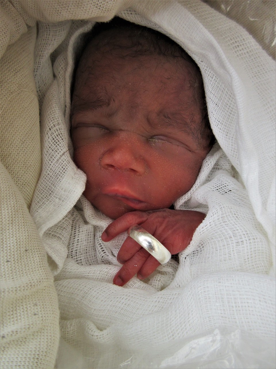A newborn baby with a wedding ring around her fingers to show how small she is