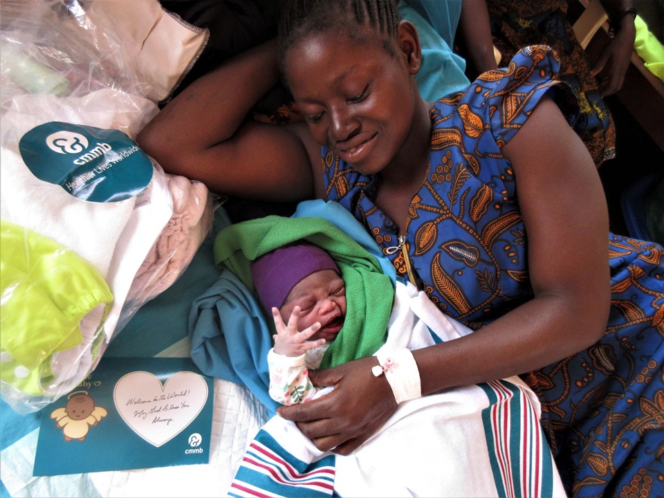 A mother in a hospital bed wit her newborn and a newborn kit provided by CMMB.