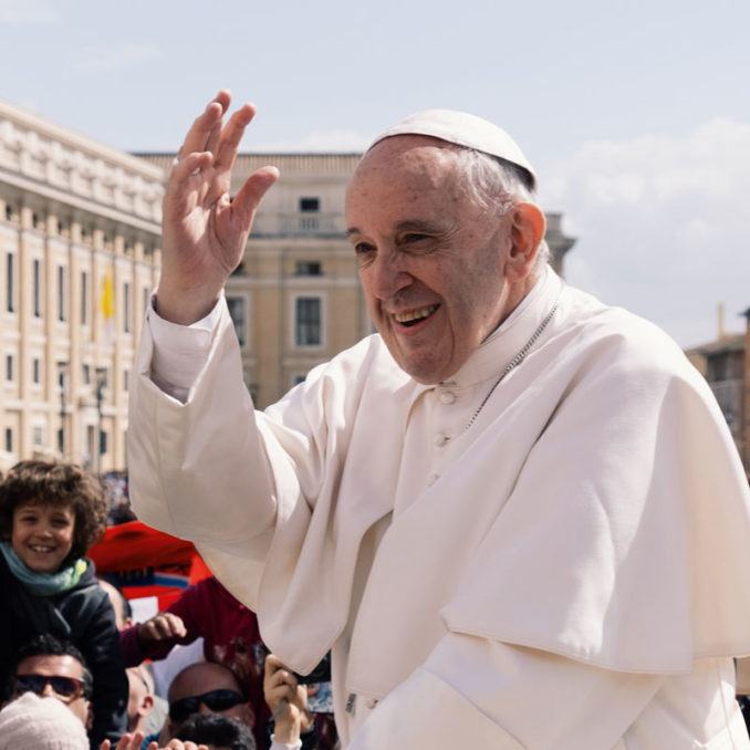 Pope Francis smiling and waving to a crowd in Vatican City in 2018.