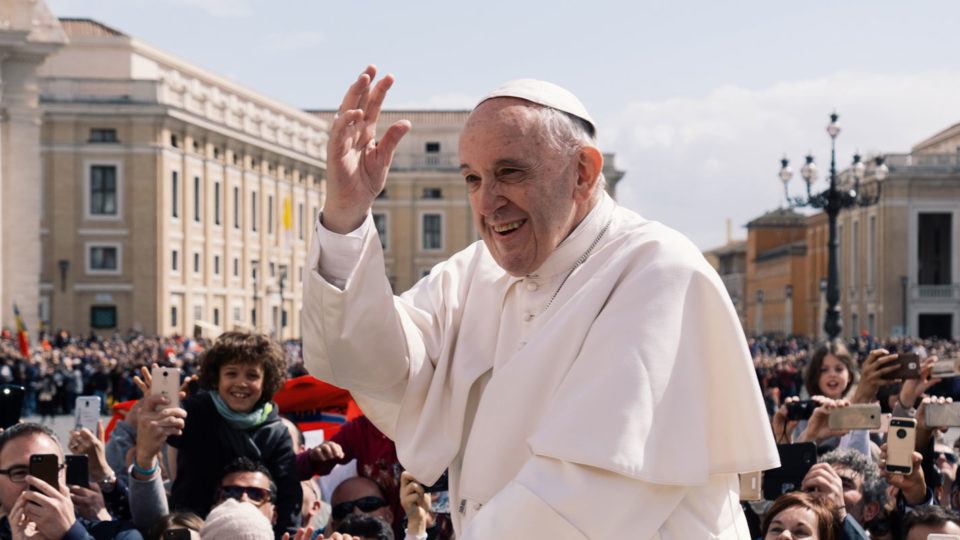 Pope Francis smiling and waving to a crowd in Vatican City in 2018.