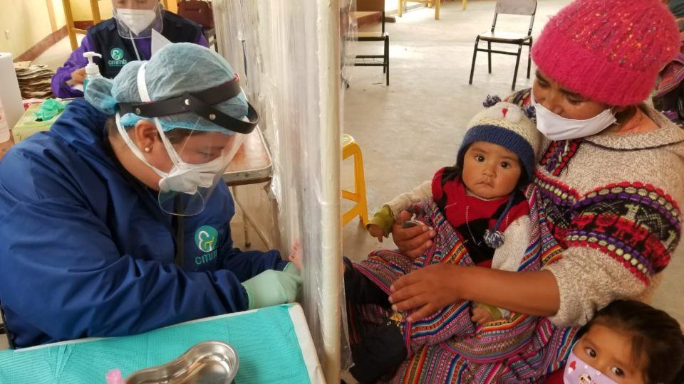 A community health worker providing care to a mother and her children during COVID-19 in Peru.