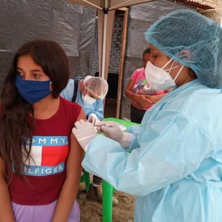 A community health worker wearing PPE during COVID-19 providing care to a young girl in Peru.