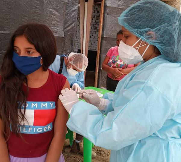 A community health worker wearing PPE during COVID-19 providing care to a young girl in Peru.