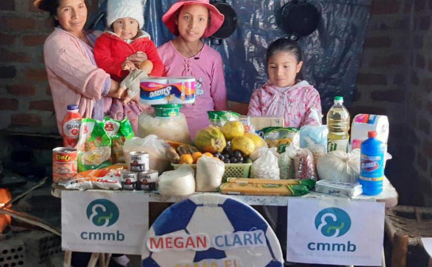 A mother with her young children stand before a survival care package for COVID-19 provided by CMMB in Peru in 2021.