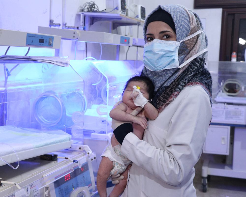 A health worther at Al-Rahma Hospital in northwest Syria hold a newborn infant in 2021.