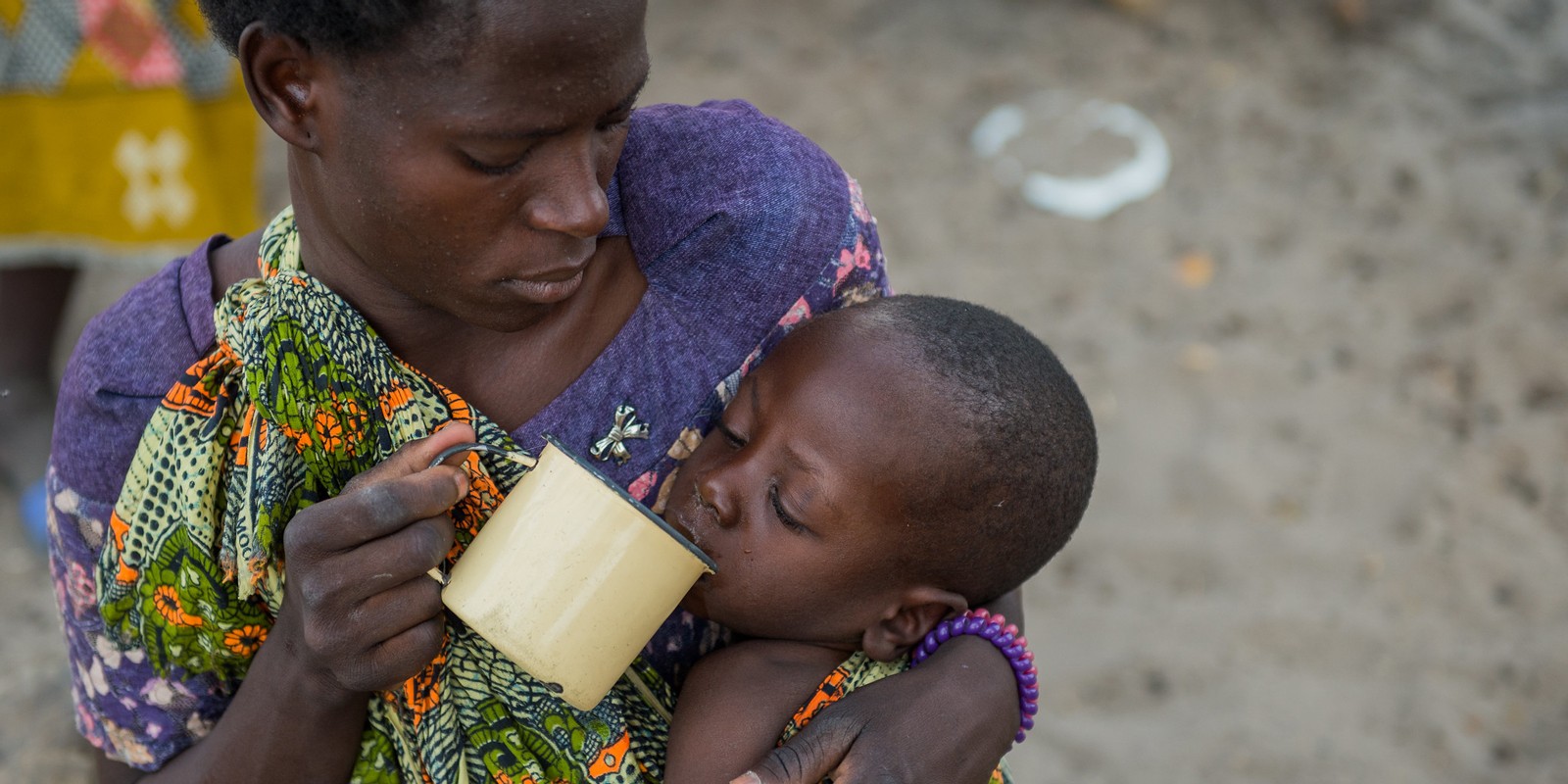A mother holds a cup feeding her malnourished child in Mwandi, Zambia in 2019.