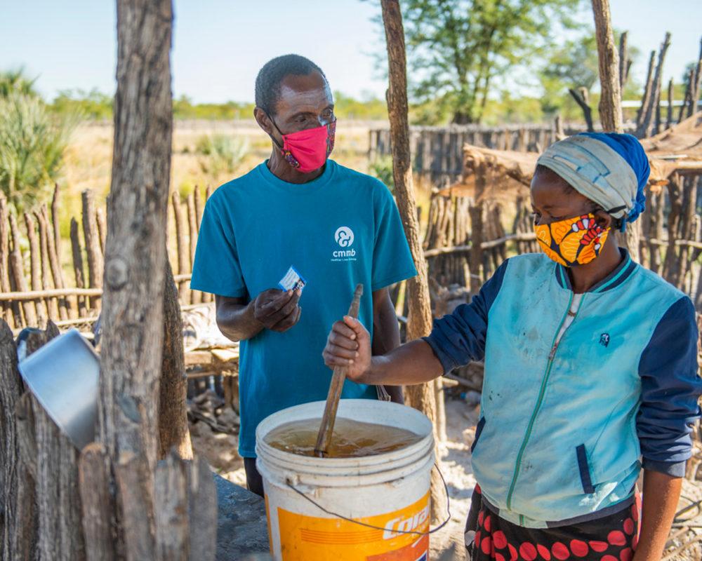 Community-Health-Worker-Woman-Clean-Water-Purification-Mwandi-Zambia-June-2021 A community health worker shows a woman how to use P&G water purification packet in Mwandi, Zambia in 2021.
