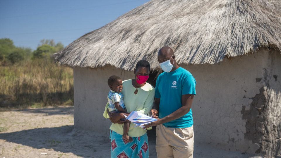 community health worker with mother and child in front of facility in zambia