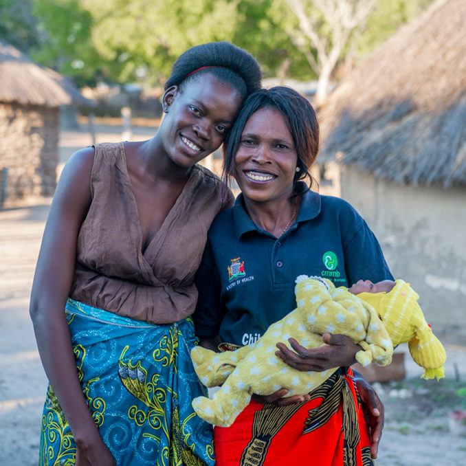 Mother-Community-Health-Worker-Baby-Rural-Mwandi-Zambia-June-2021 A mother with a community health worker holding an infant in rural Mwandi, Zambia in June 2021.