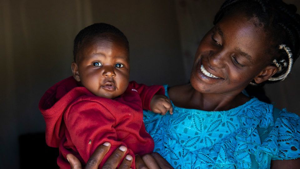A mother holding her smiling baby girl in Zambia in May 2021.