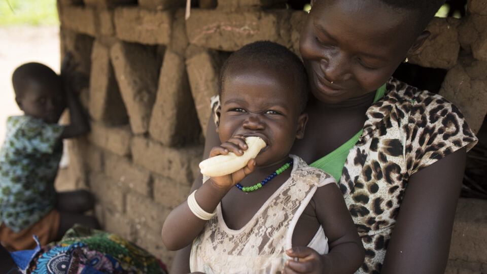 south sudan child eating banana with mother at home