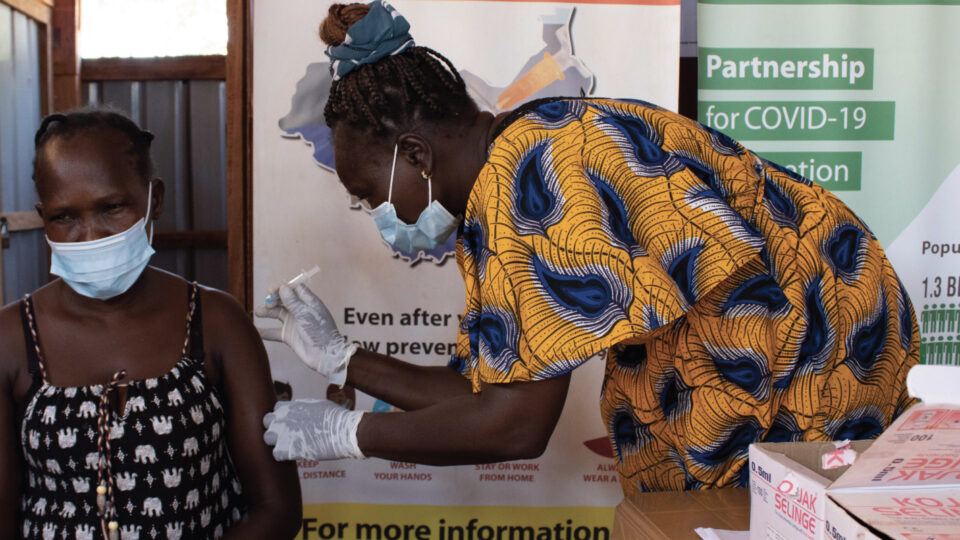A CMMB health worker administering a COVID-19 vaccine to woman in South Sudan in December 2021.