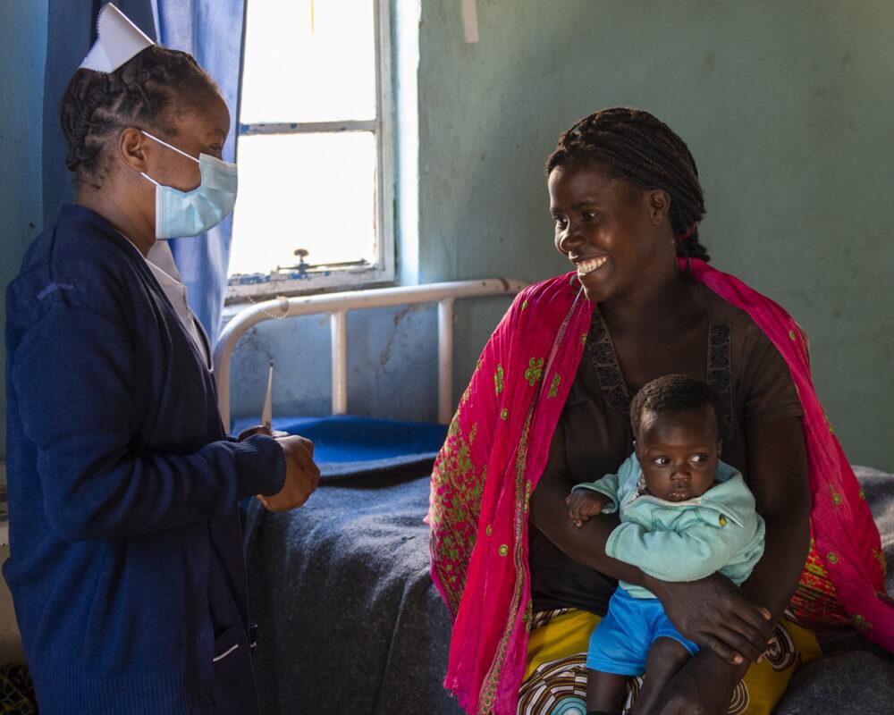 A community health worker with a mother and child at a health facility in Zambia in May 2021.