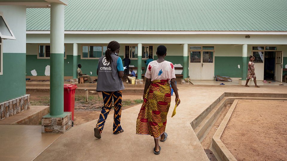 A-CMMB-staff-member-and-patient-on-the-grounds-of-St.-Theresa A CMMB staff member and patient walk towards St. Theresa Hospital