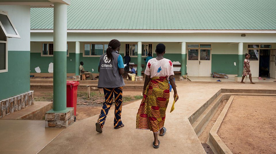 A CMMB staff member and patient walk towards St. Theresa Hospital