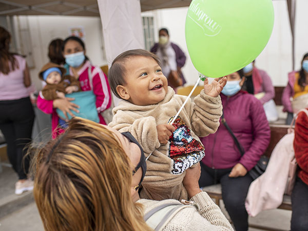 Community-health-event-iCMMB-Peru A baby smiles while holding a green balloon at a community event in Peru.