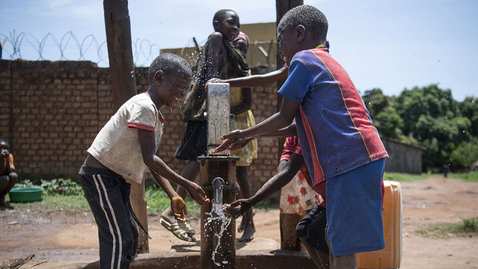 Children collect and play in water at the water pump.