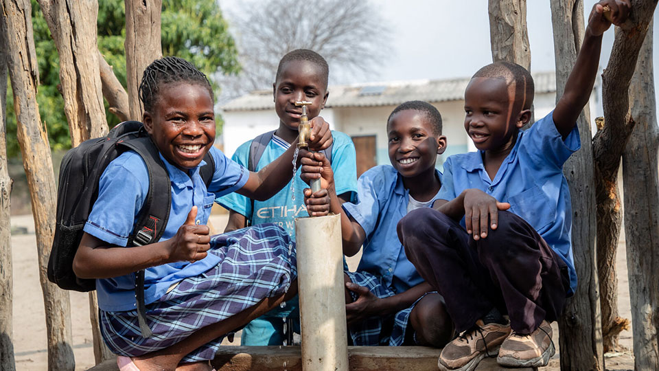 Children smile around the water pump installed by CMMB Sept 2025