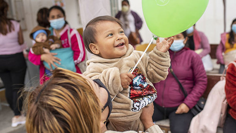 a baby smiles up at a green balloon. 