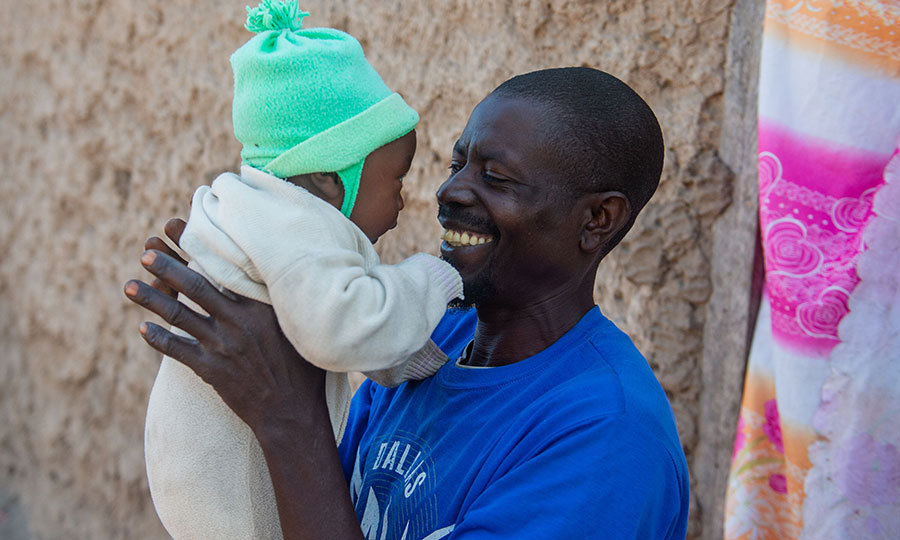 A father holds his baby and smiles