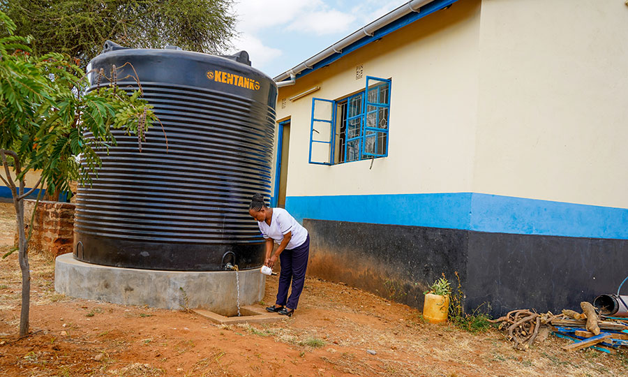 A health worker fills a cup with water from a rainwater catchment tank.