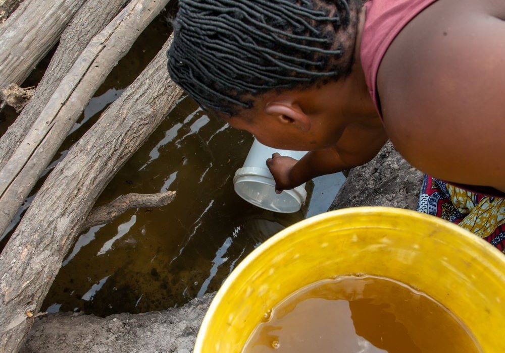 a woman reached into a shallow water well to collect water for her day